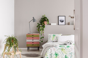 Urban jungle in grey scandinavian bedroom with wabi sabi nightstand and bed with floral duvet and...