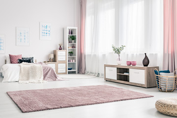 Big fluffy rug on white wall of classy bedroom interior with wooden cabinet and wicker basket