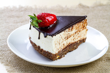 A slice of sweet cake with whipped cream, fresh strawberries and dripping chocolate glaze in a white plate
