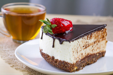 A cup of hot tea and a slice of sweet cake with fresh strawberries and dripping chocolate glaze in a white plate. Sweet dessert