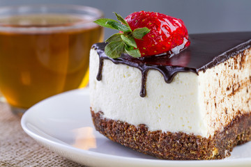A cup of hot tea and a slice of sweet cake with fresh strawberries and dripping chocolate glaze in a white plate. Sweet dessert