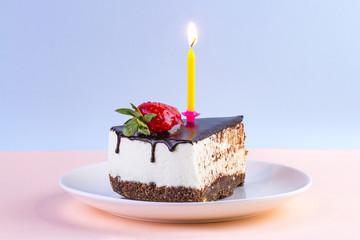 Strawberry cake with dripping chocolate glaze and a lit candle in a plate on a colorful background...