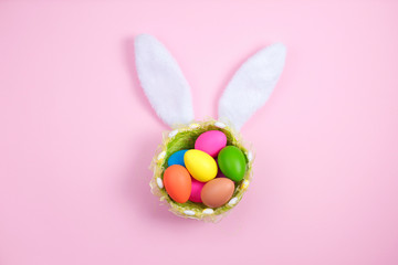 Happy easter with adorable bunny ears on basket full of Easter eggs on pink background