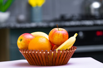 Fresh fruits - orange, banana, apples in a wooden bowl in a kitchen at home.