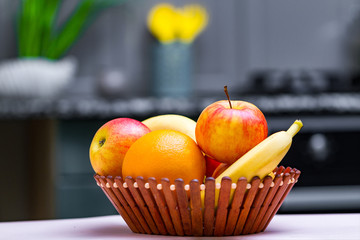 Fresh fruits - orange, banana, apples in a wooden bowl in a kitchen at home.
