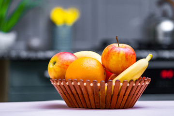 Fresh fruits - orange, banana, apples in a wooden bowl in a kitchen at home.