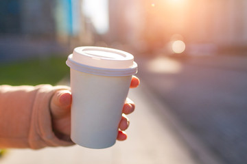 Young woman in casual clothes holding paper coffee cup and enjoying the walk in the city in the morning on a sunny day. Coffee away and to go