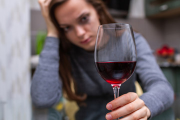 Depressed, divorced crying woman sitting alone in kitchen at home and drinking a glass of red wine because of problems at work and troubles in relationships. Social and life problems
