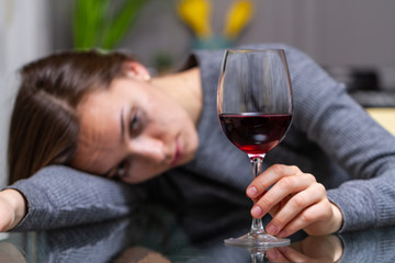 Depressed, divorced crying woman sitting alone in kitchen at home and drinking a glass of red wine because of problems at work and troubles in relationships. Social and life problems