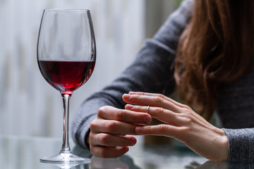 Divorced woman pulling wedding ring from finger and drinking a glass of a red wine because of adultery, betrayal and a failed marriage. Divorce concept. Relationship and love end. Life problems