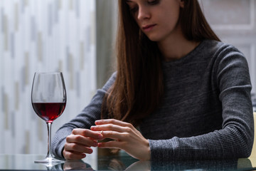 Divorced woman pulling wedding ring from finger and drinking a glass of a red wine because of adultery, betrayal and a failed marriage. Divorce concept. Relationship and love end. Life problems