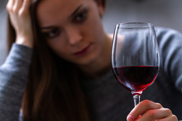 Depressed, divorced crying woman sitting alone in kitchen at home and drinking a glass of red wine because of problems at work and troubles in relationships. Social and life problems