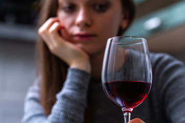 Depressed, divorced crying woman sitting alone in kitchen at home and drinking a glass of red wine because of problems at work and troubles in relationships. Social and life problems