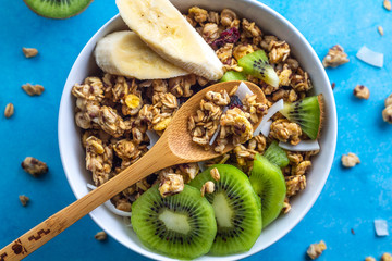 Dry breakfast cereals. Crunchy honey muesli bowl with slices of fresh banana and kiwi on a blue background. Raw diet and fiber food. Top view. Breakfast time