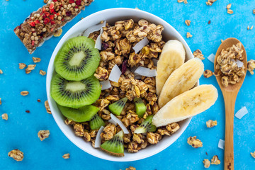 Dry breakfast cereals. Crunchy honey muesli bowl with slices of fresh banana and kiwi on a blue background. Healthy, fitness and fiber food. Top view. Breakfast time