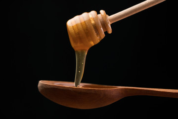 A wooden spoon scoops up the honey flowing from it on a dark background. Close-up.