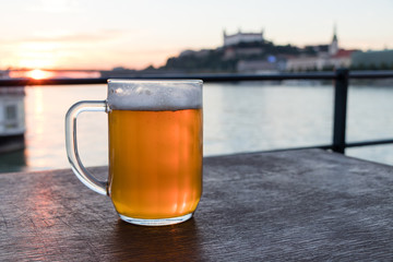 Slovak beer 0,5 liter on wooden table on the background the river Danube and Bratislava castle at sunset, Slovakia
