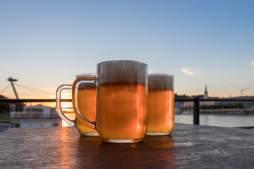 Three light beer glasses on the wooden table on background sky and sunset