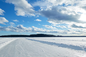 Slippery road on the ice of frozen lake on a sunny winter day in Finland. White snow and clouds on blue sky.Beautifull winter landscape.
