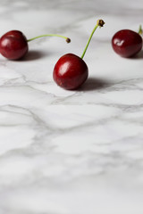 Three cherries, one of them focused on white marble background with copy space