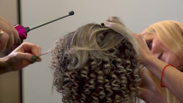 Makeup artist at work, hairdresser makes laying blond curls of young girl