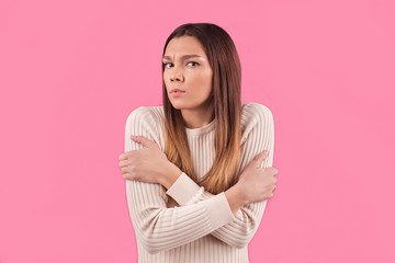 Obraz premium Dissatisfied woman feels cold during freezing chilly weather, hugs herself and clenches teeth, feels discomfort, afraids of something, isolated over pink background. Close up shot