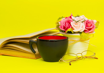 Black cup with hot tea and book on the yellow background