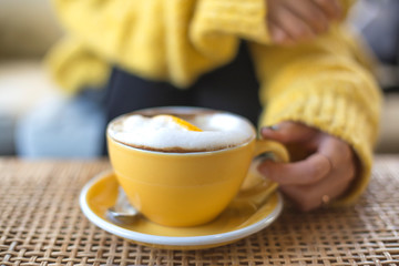 Young pretty woman in wool sweater with yellow coffee cup in hands