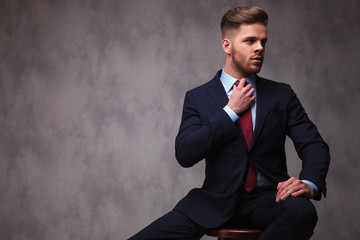 seated businessman looks to side while fixing red bowtie