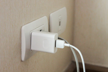 smartphone charging adapter plugged on electric socket on wall