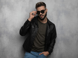 portrait of seductive relaxed man in leather jacket arranging sunglasses