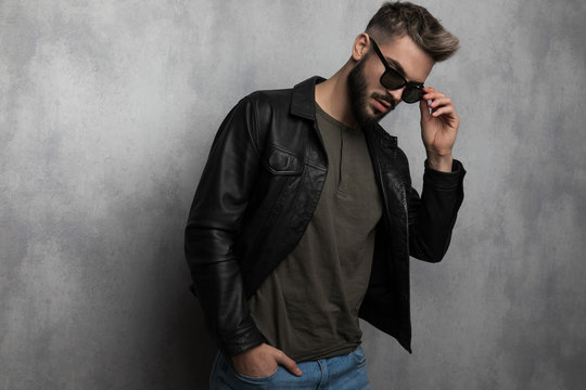 portrait of sexy relaxed man in leather jacket fixing sunglasses