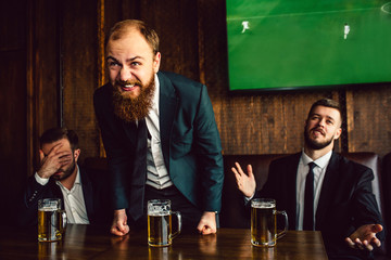 Young man in middle stand and lean forward. He is happy. Other two men are upset and unhappy. Guy on left hold hand on face.