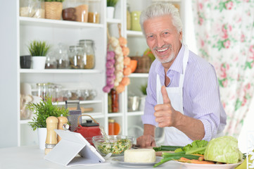 Portrait of senior man showing thumb up while preparing dinner in kitchen