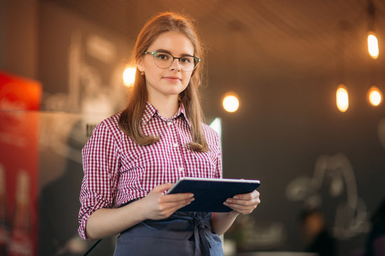 Attractive young waitress using a tablet computer to take an order from a customer in a coffee shop