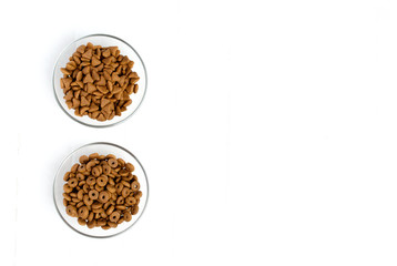 Dry cat food poured into a glass bowl on a white background