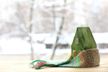 layout of green paper house in scarf against the background of a blurred winter landscape . environmental technologies for a comfortable stay