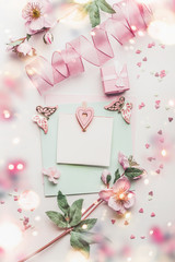 Lovely greeting card composition in pastel color with mock up, flowers and little gift box, hearts and handicraft decoration accessories, top view