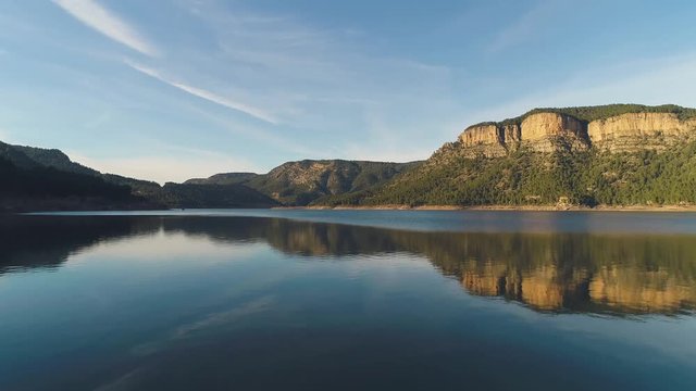 Aerial: Low Angle Lake Surrounded By Hills And Mountains Covered In Woods. Dramatic Golden Hour Light. Clear Mountain Peak Reflection In The Still Water