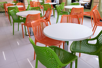 Orange and green chairs around white tables. A modern interior of food court in a mall, cafe, airport or family fast food restaurant without people. Copy space.
