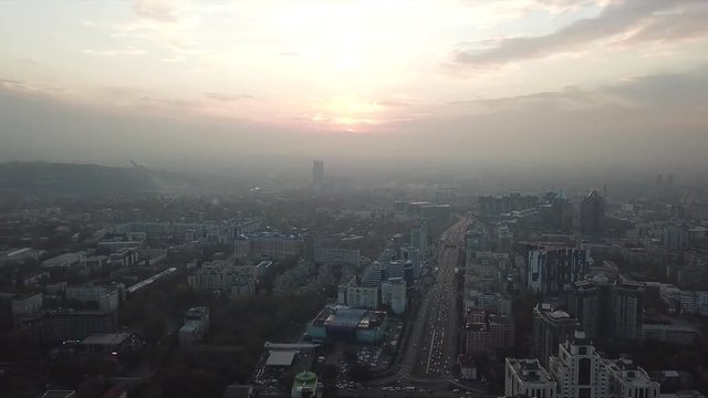 Shooting from a drone over the big city of Almaty. View of many roads, cars, people and large mountains. Places smog and fog. People walk the streets. Beautiful buildings with glass Windows. Trees.