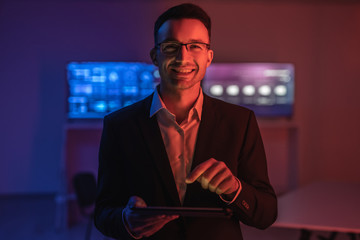 The happy man in glasses working with a tablet in the dark room