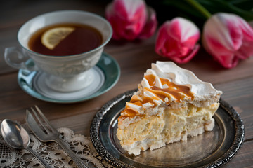 Slice of meringue cake and a cup of tea and tulips on the table