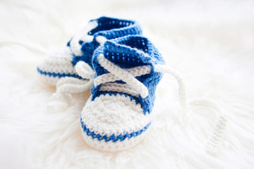 Little baby shoes. Handknitted first sneakers for newborn boy or girl. Crochet handmade bootees on fluffy white background.