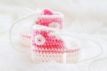 Little baby shoes. Hand knitted first sneakers for newborn  girl. Crochet handmade bootees on fluffy white background.
