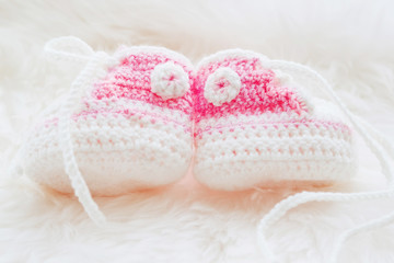 Obraz na płótnie Canvas Little baby shoes. Hand knitted first sneakers for newborn girl. Crochet handmade pink bootees on fluffy white background.
