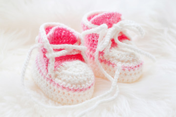 Fototapeta na wymiar Little baby shoes. Hand knitted first sneakers for newborn girl. Crochet handmade pink bootees on fluffy white background.
