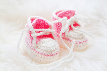 Little baby shoes. Hand knitted first sneakers for newborn  girl. Crochet handmade pink bootees on fluffy white background.