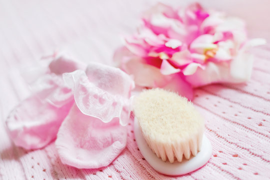 First accessories for newborn girl - pink booties, hat with silk flower and tiny hair brush. Cute pink background.