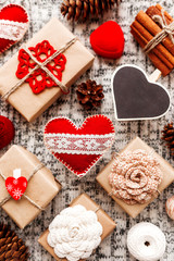 Valentine's Day symbols - hearts, presents in craft paper with crochet flowers, pine cones, red jewelry gift box - on knitted background.